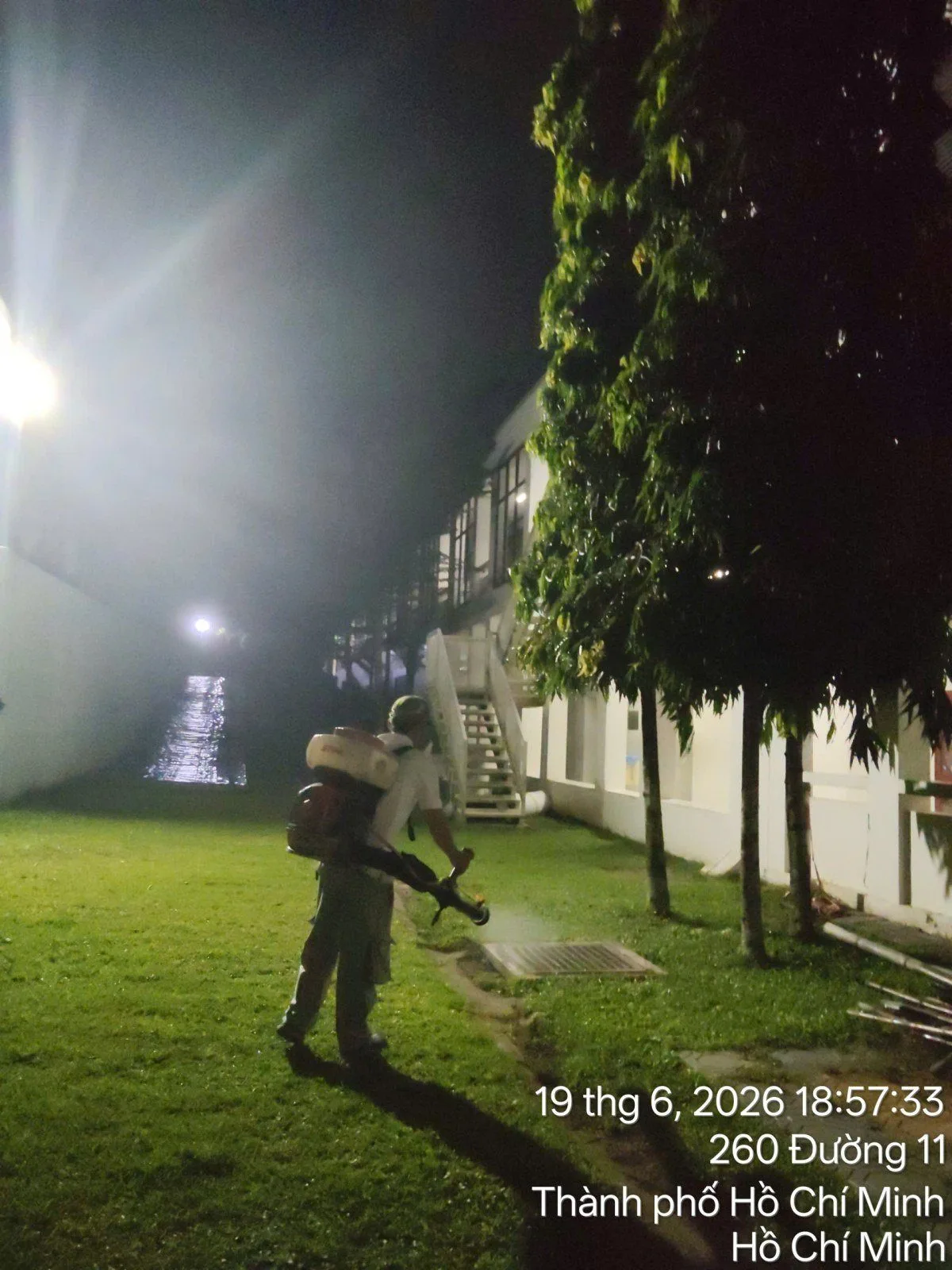 A technician treating a school yard for mosquitoes at night under the lights