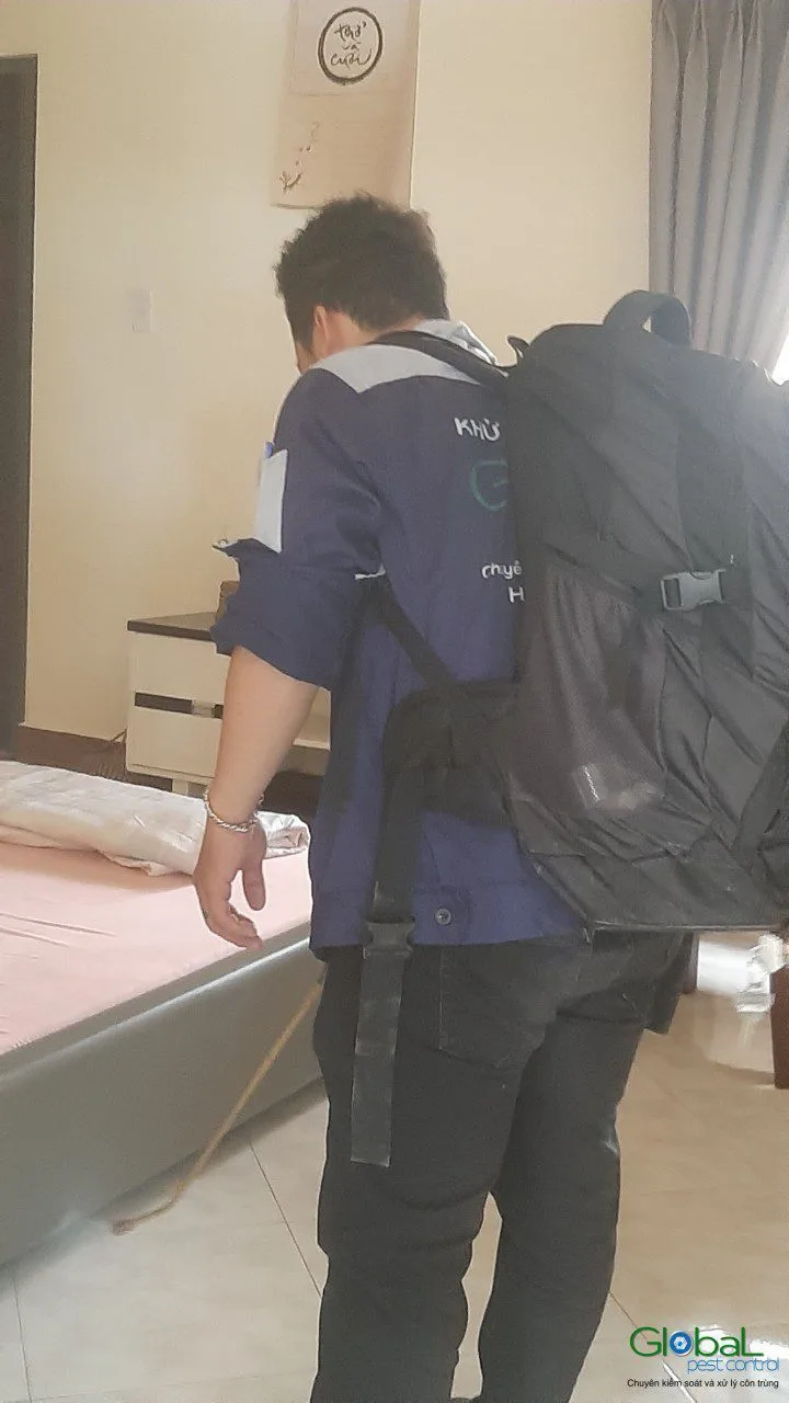 A technician carrying a sprayer into a bedroom cleared of mattresses