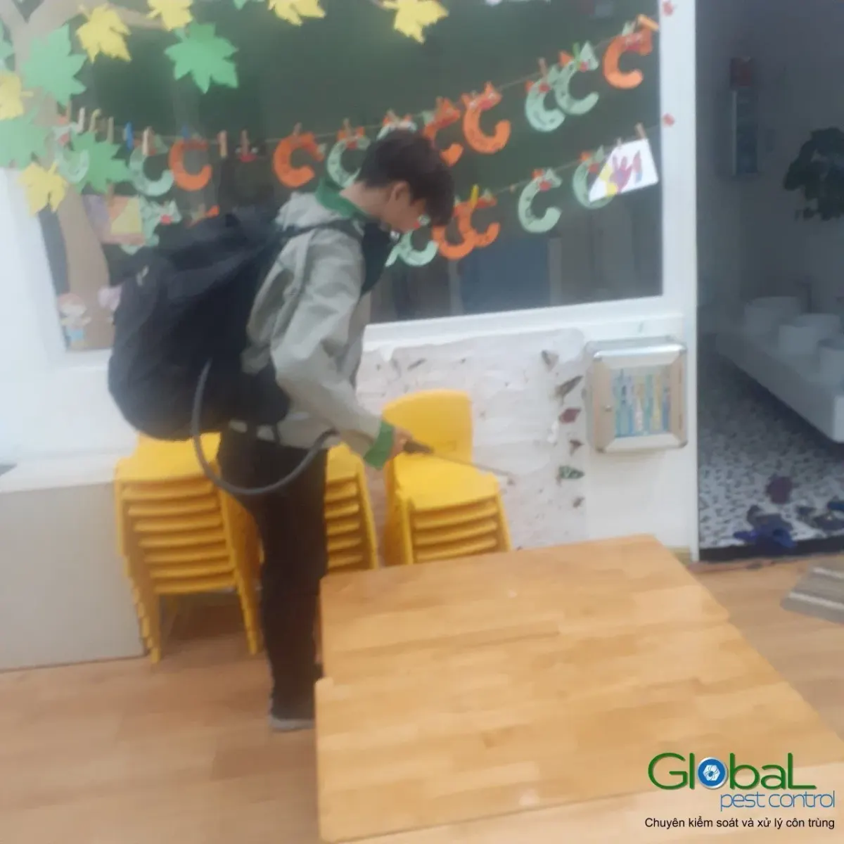 A technician treating around stacked plastic chairs in a kindergarten