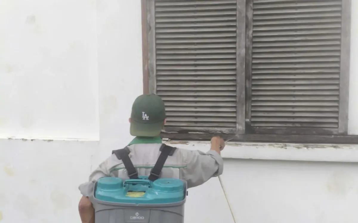 A technician treating around the wall base and ground-floor windows of a house