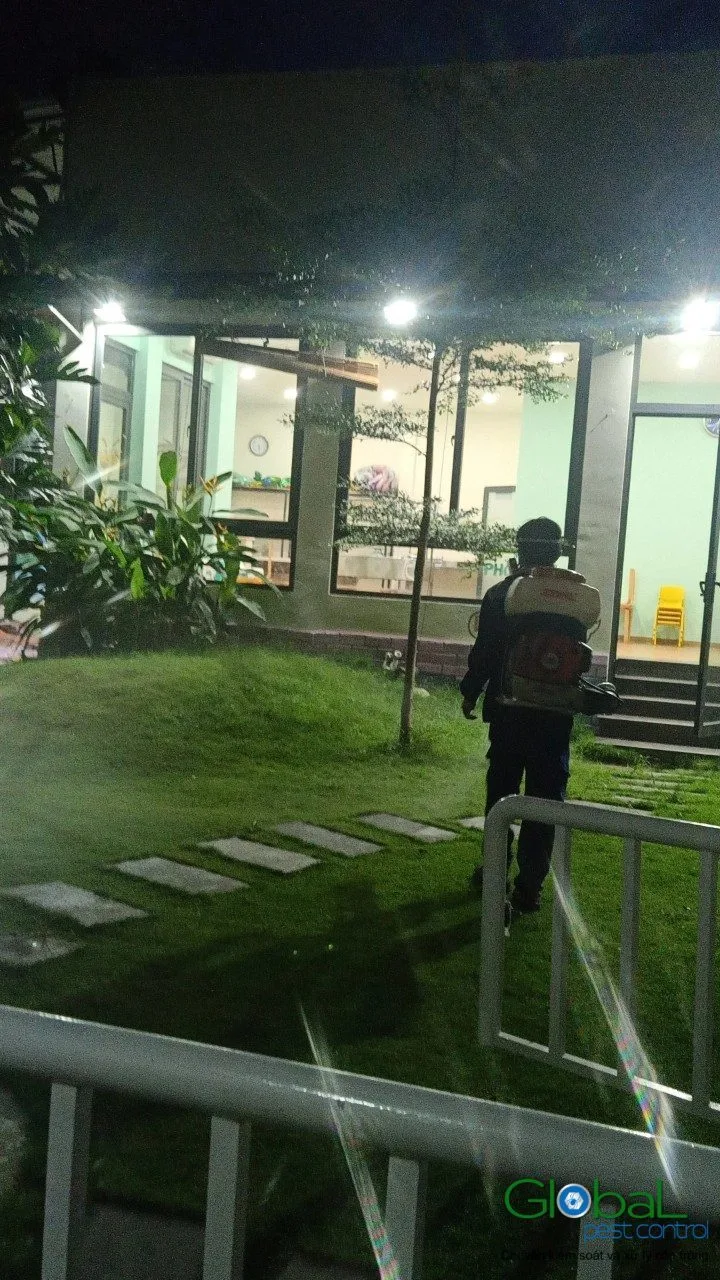 A technician treating a factory garden for mosquitoes at night