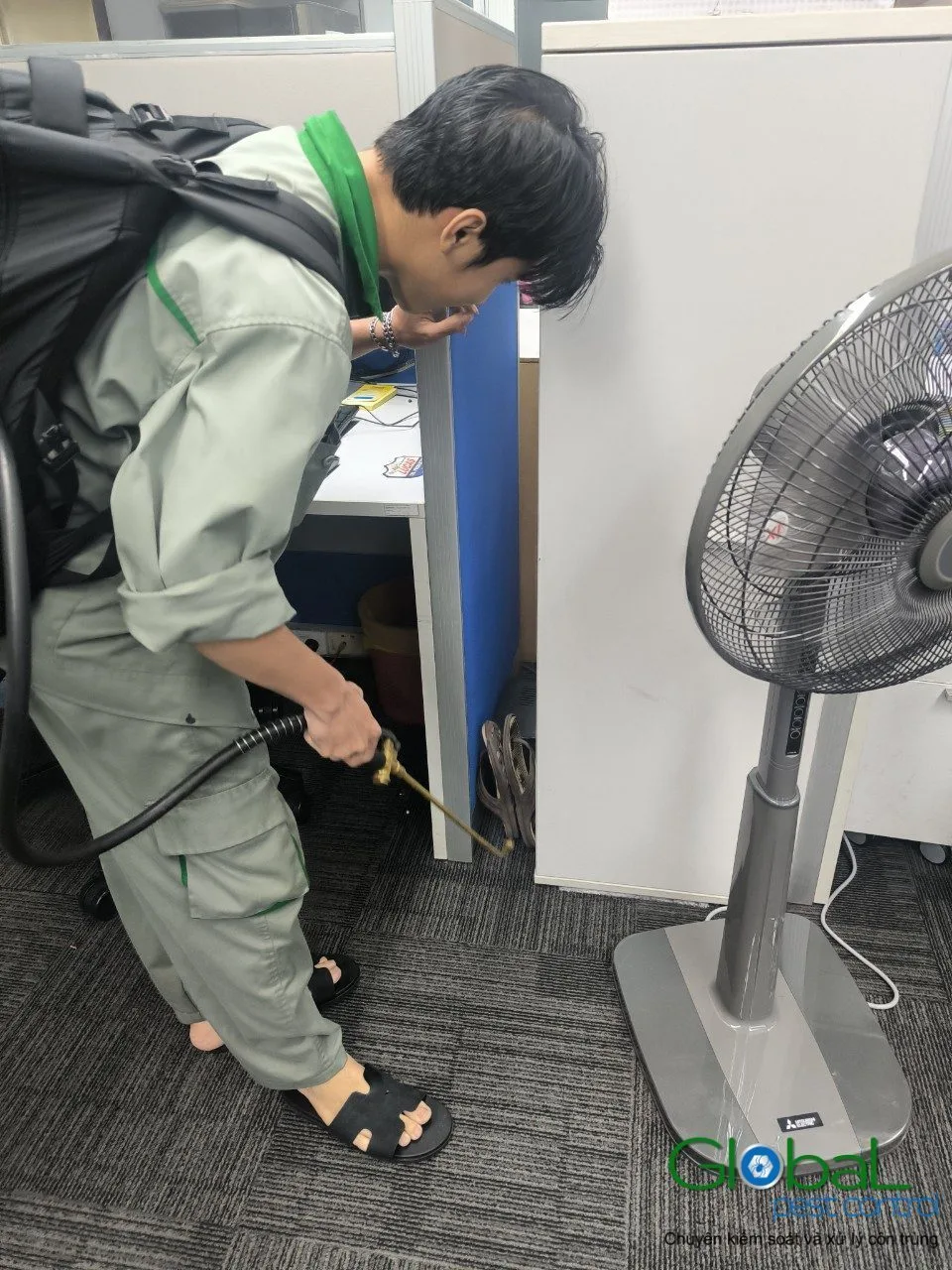 A technician treating cabinet gaps beside a standing fan in an office