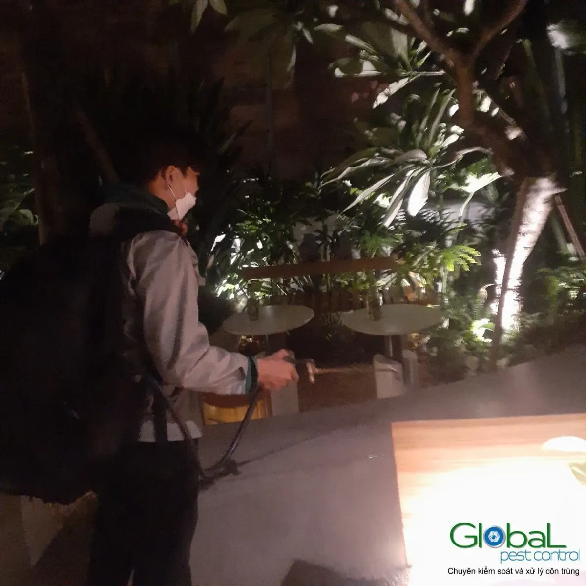 A technician treating around garden planters at an eatery at night