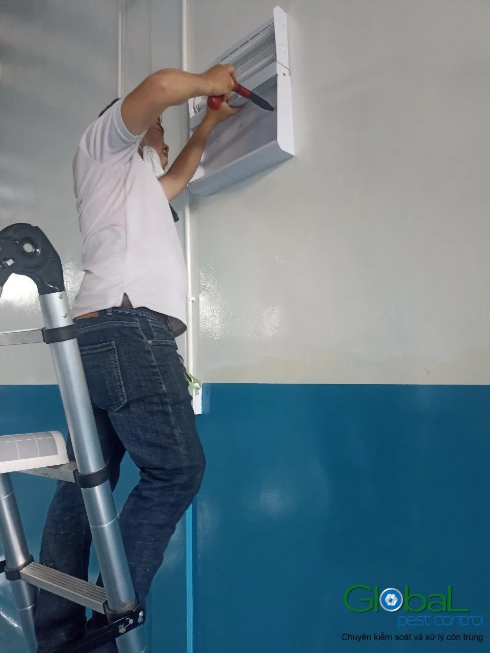 A technician on a ladder fitting a fly light in a food factory