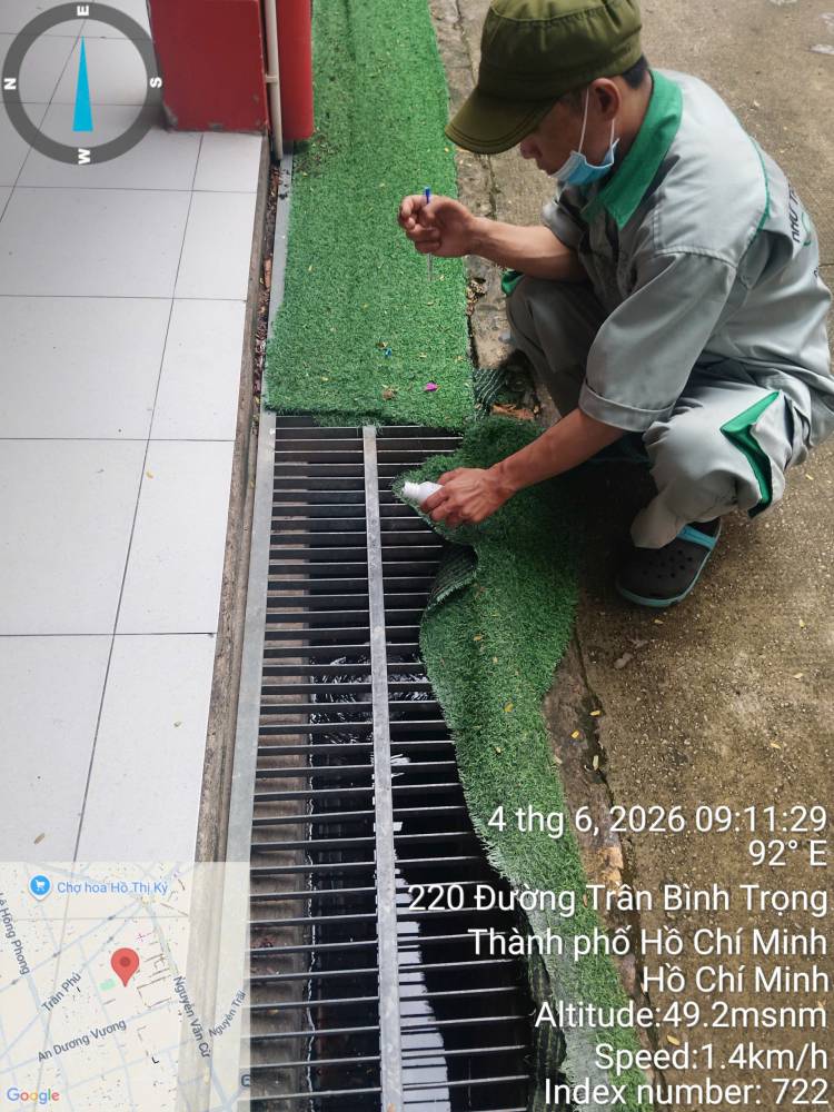 A technician lifting a drain grate and treating the gully beneath it